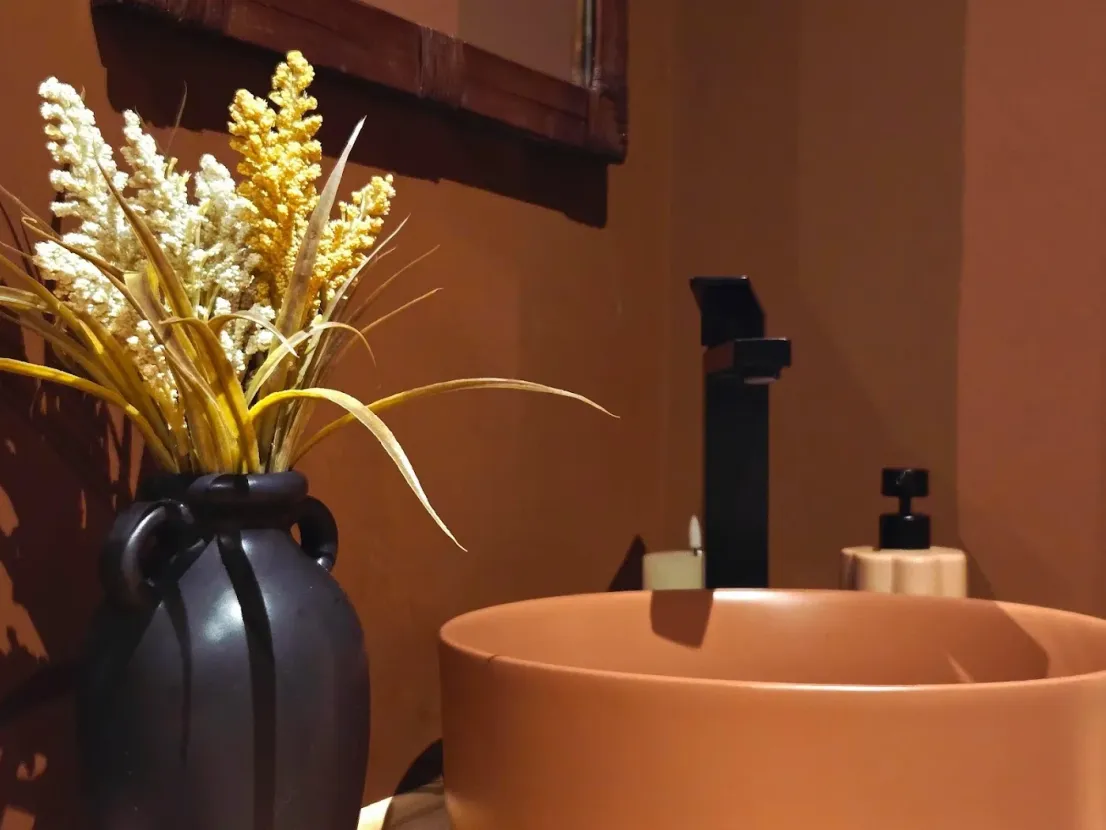 El baño: lavabo redondo de terracota y un jarrón negro con flores secas.